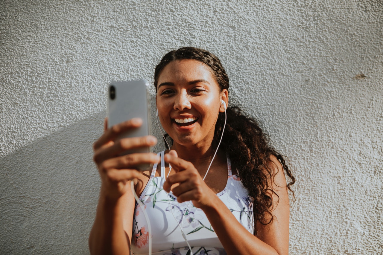 Woman Using Silver Iphone X While Leaning on Wall and Smiling