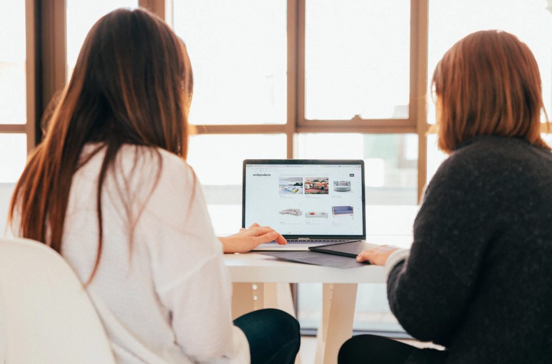 two people sitting at a table looking at a laptop.