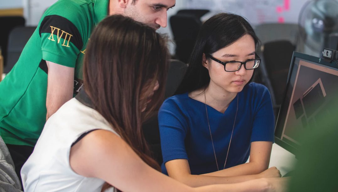 Three people working together looking at a computer screen.