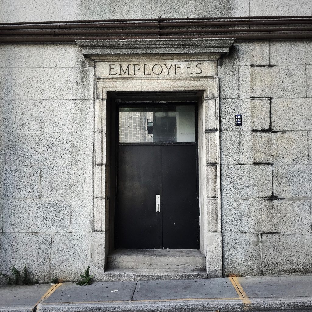 Photo of an entrance to a stone building. The word "employees" is written above the door frame.