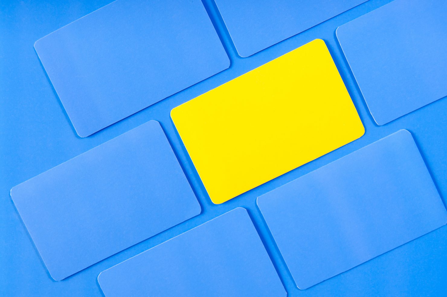Photo of multiple square pieces of paper turned at an acute angle. All of the pieces of paper are blue save one in the middle which is yellow. This photo represents the importance of consistent visual branding.